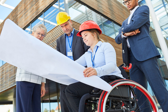 Disabled woman as an architect in a wheelchair with blueprint together with engineers