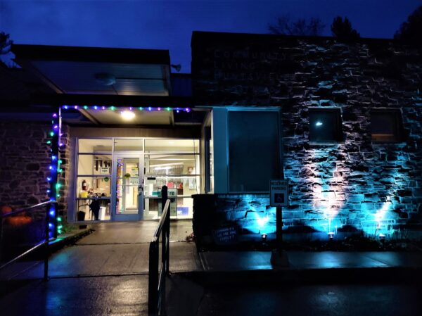 Night-time shot of the Huntsville Community Living Offices. There is a string of purple and blue lights on the building entrance, and the front wall glows blue from a blue spotlight.