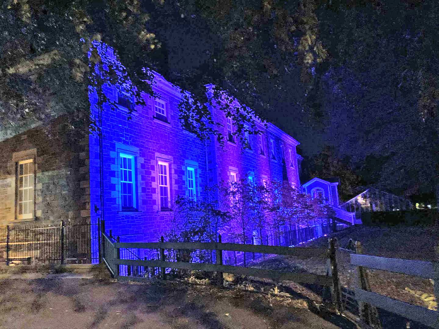 A photo of Government House in St. John's. The exterior wall and windows near to the camera are glowing purple and blue.