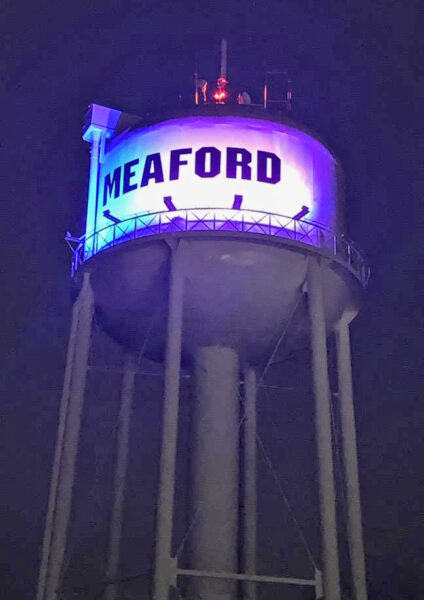 A looking-up shot of the municipal water tower in Meaford, Ontario. The tower reservoir is glowing purple and blue from the tower lighting.