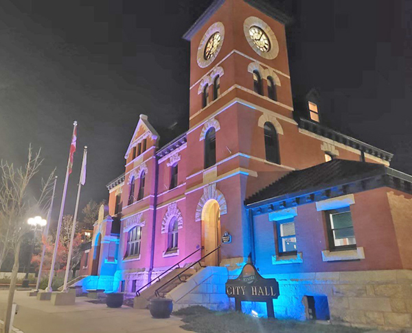 Exterior purple and blue spotlights shine on the walls of Kenora City Hall.