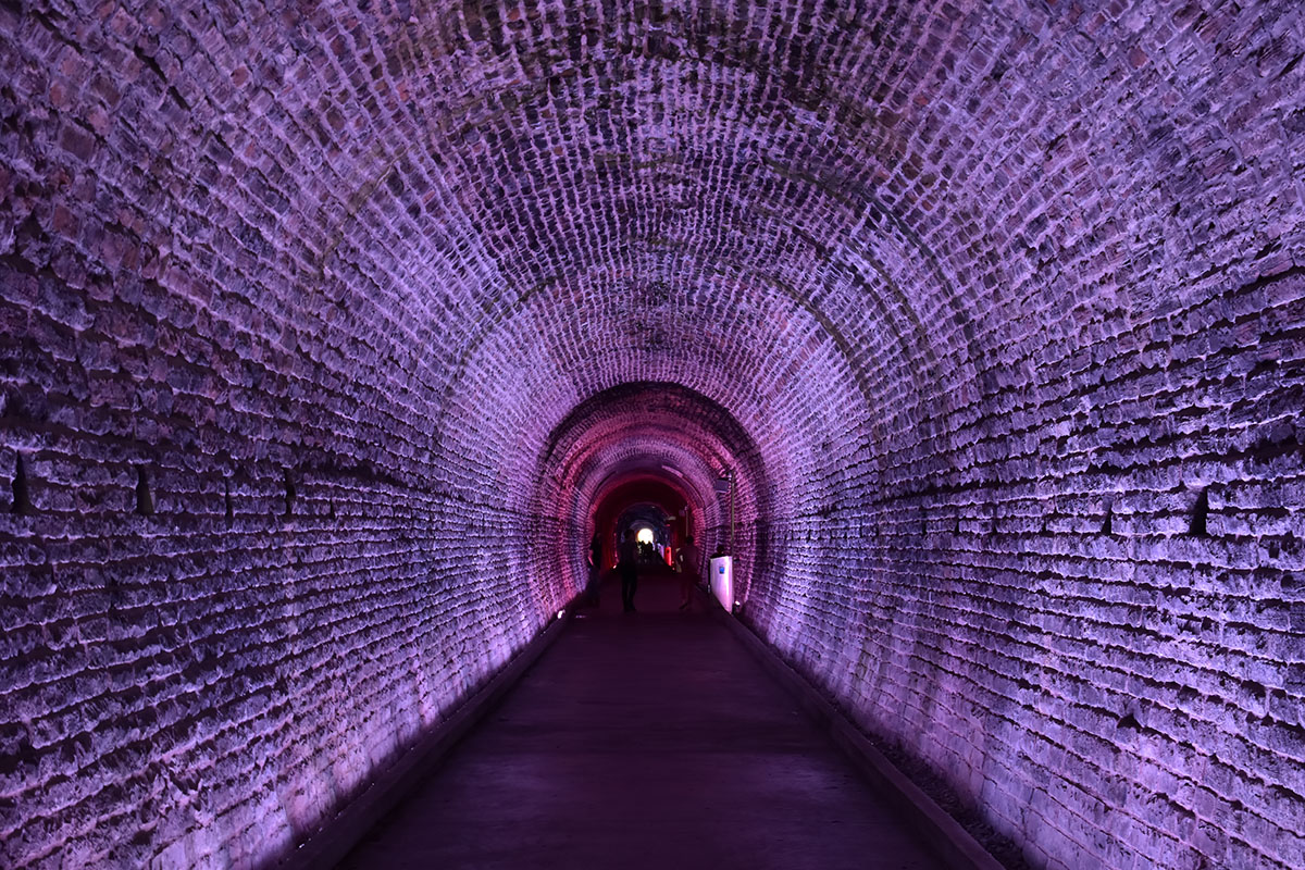 Looking down the walkway inside an old brick railroad tunnel that's illuminated purple.